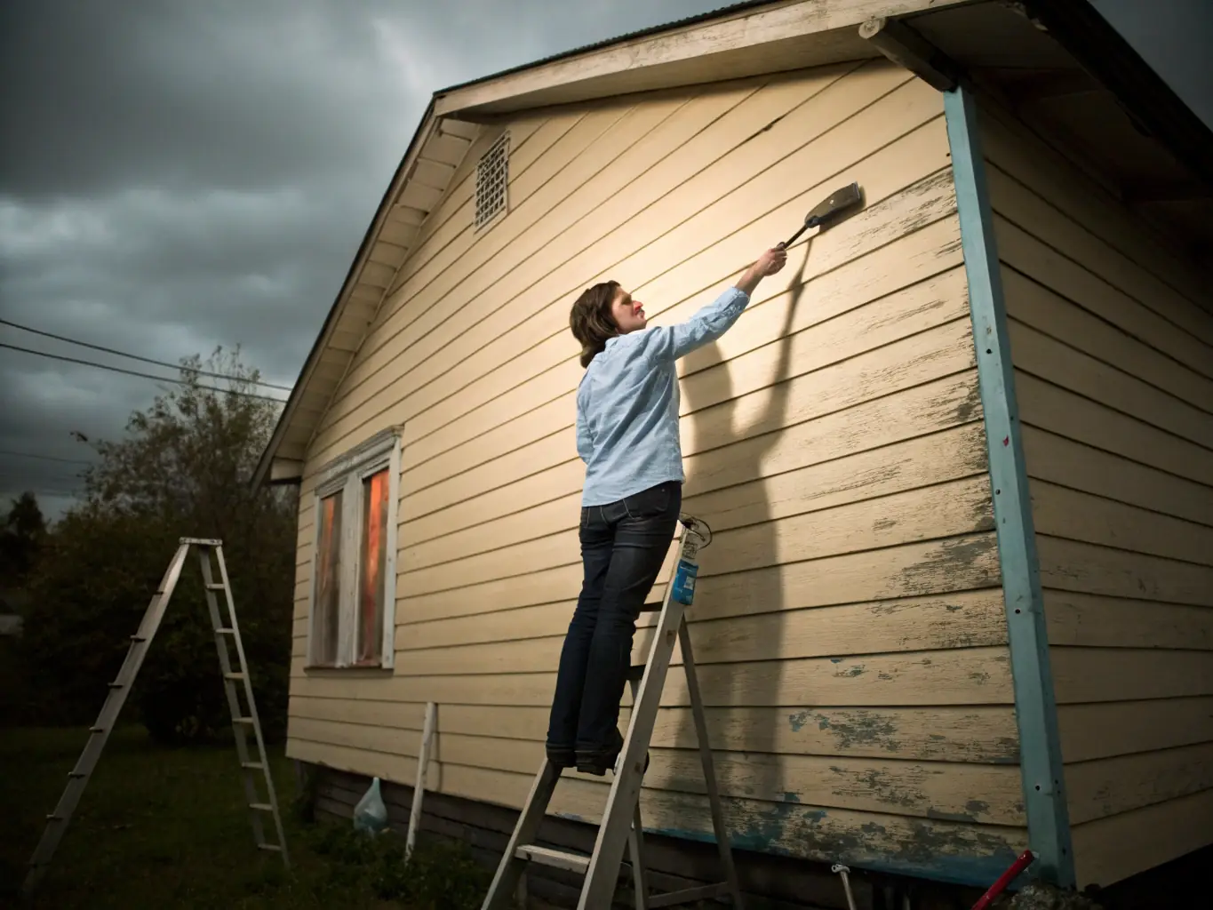 A painter carefully applying a fresh coat of paint to a building facade, highlighting the transformative effect of professional painting services.